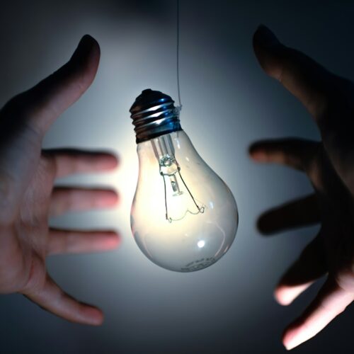 Two hands reaching towards a light bulb in a dark setting, symbolizing ideas or innovation.